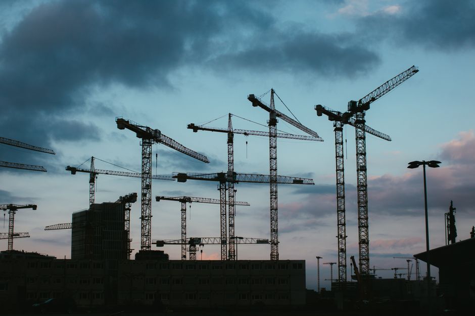 Multiple construction cranes silhouetted against the evening sky